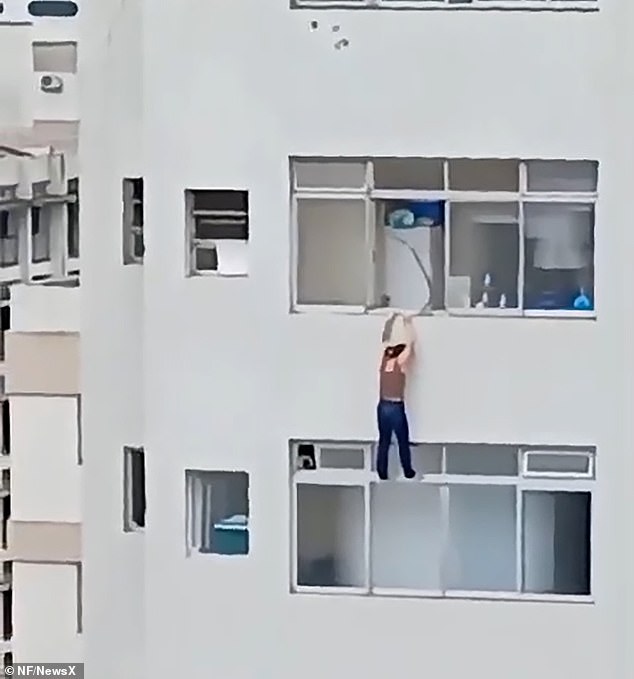 This is the dramatic moment a woman clings for her life as she dangles from the edge of a high-rise apartment building after slipping while cleaning the windows