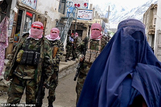 Taliban security personnel stand guard as an Afghan burqa-clad woman (R) walks down a street at a market in the Baharak district of Badakhshan province on February 26, 2024