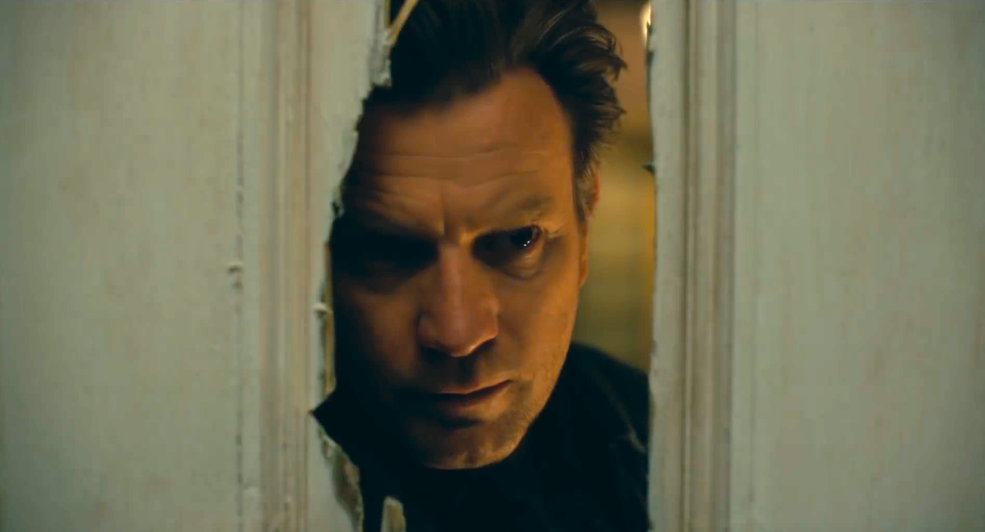 Ewan McGregor peers through a hole in a wooden door in Doctor Sleep.