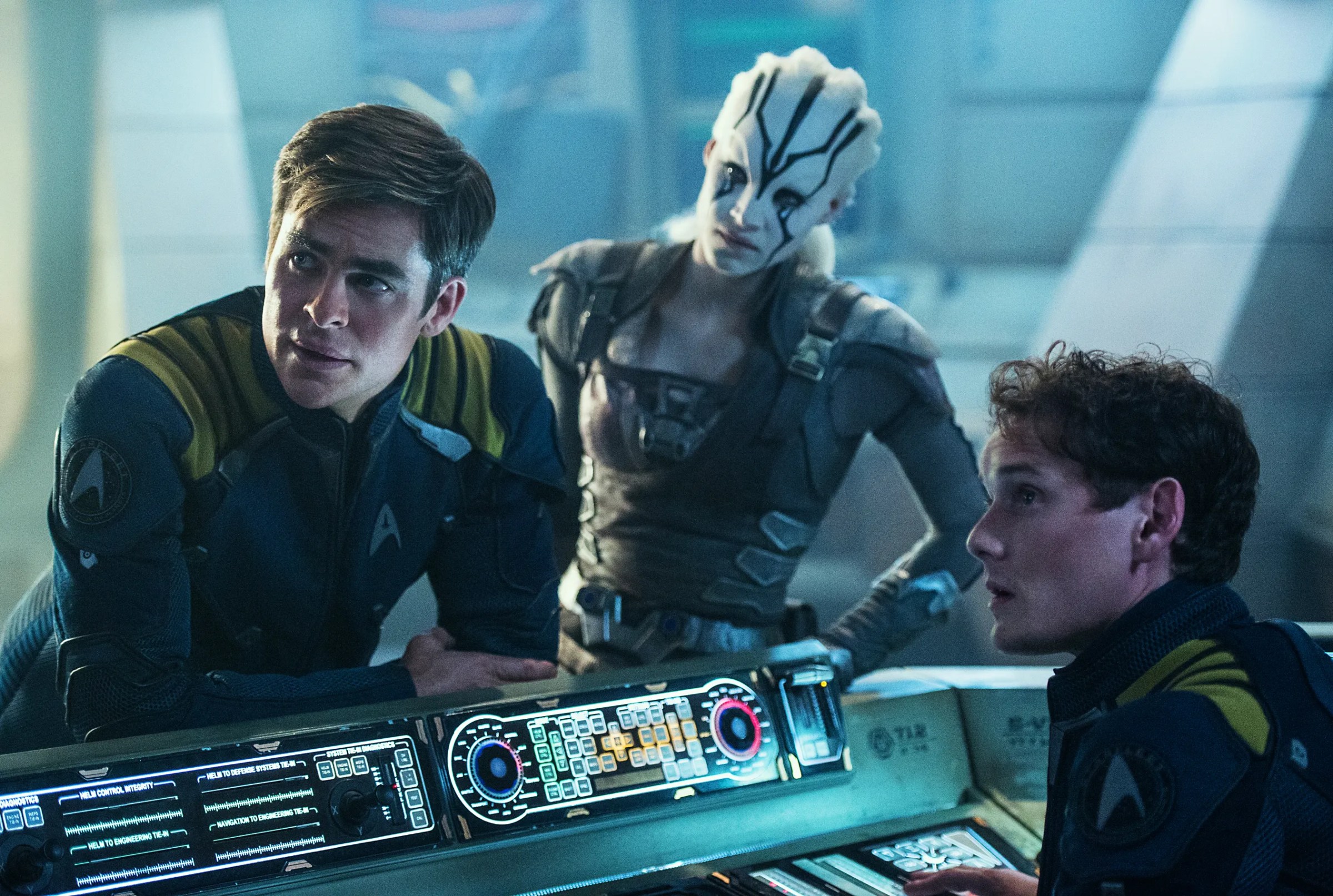 Captain Kirk (Chris Pine), Jaylah (Sofia Boutella) and Pavel Chekov (Anton Yelchin) leaning over a console in Star Trek Beyond.