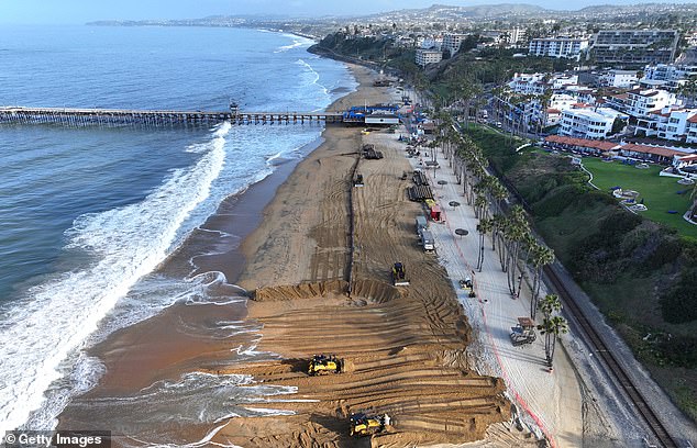 Workers move fresh sand brought by barge to the main public beach during a sand replenishment project along the eroding coastline on May 21, 2024 in San Clemente, California