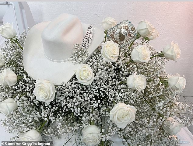 The coffin was draped with a white cloth under a bouquet of white roses and baby's breath. The arrangement was completed with a silver belt buckle and a white western hat