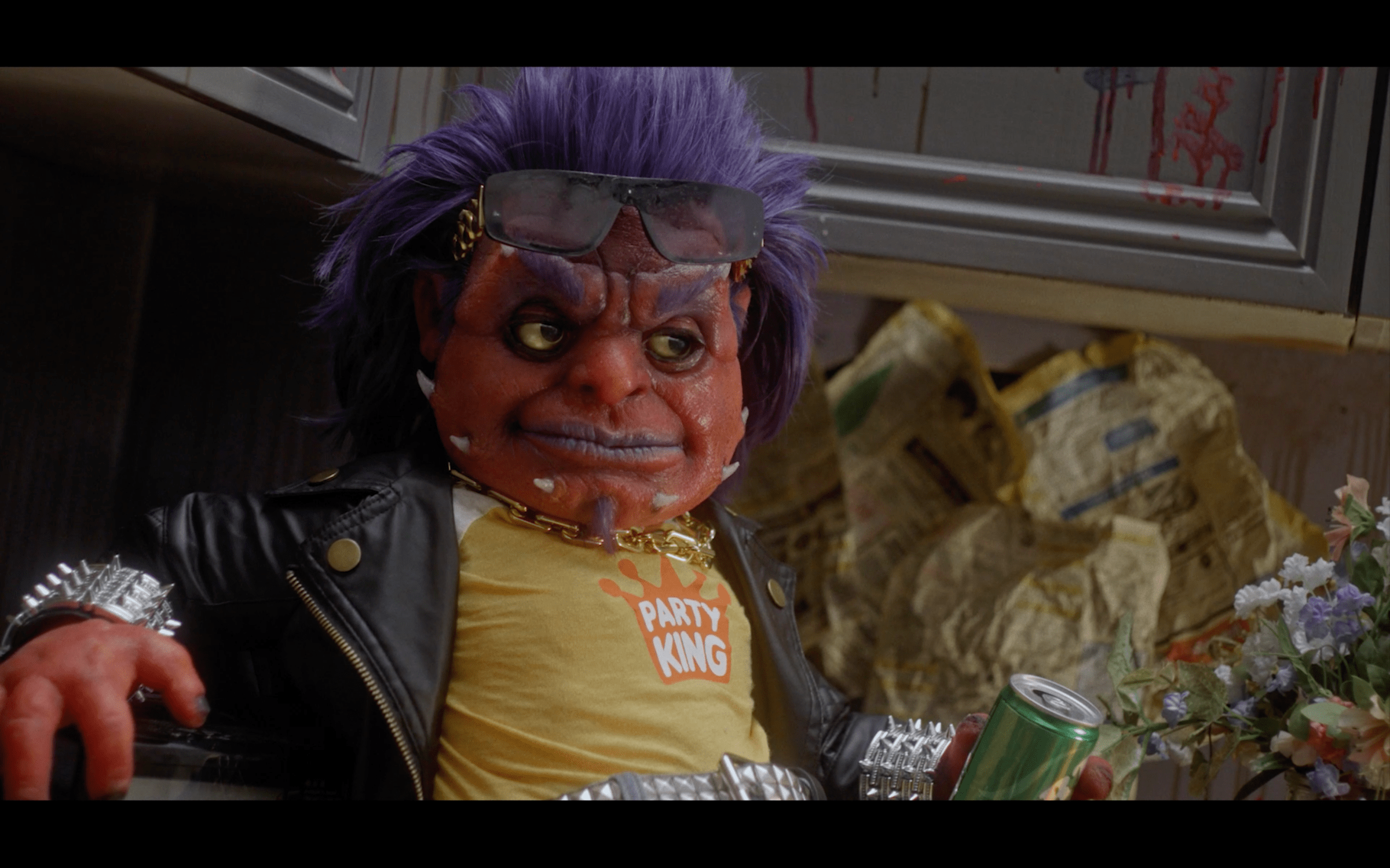 Frankie Freako, an orange gremlin-like creature in motorcycle gear, with a can of soda in a destroyed kitchen in Frankie Freako.