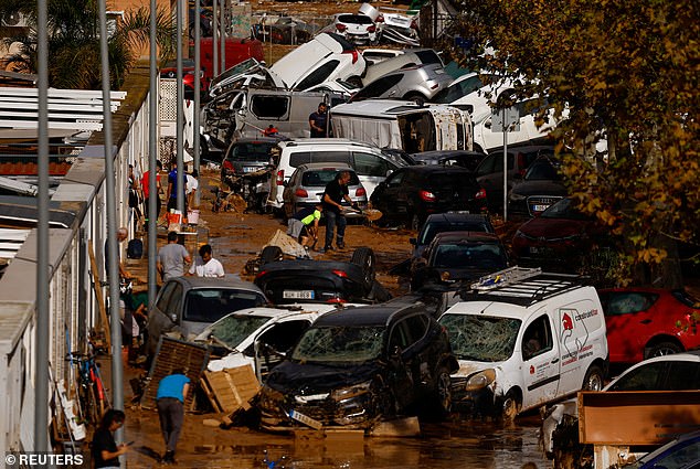 People clear a muddy street next to piled up cars after heavy rain in Alfafar, in Valencia, Spain, November