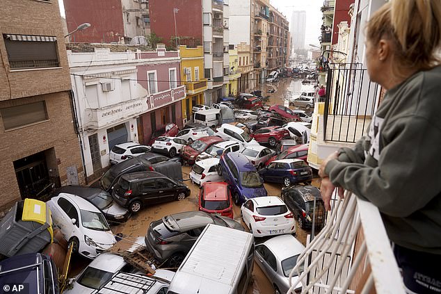 A woman looks out from her balcony as vehicles are stuck on the streets during flooding in Valencia