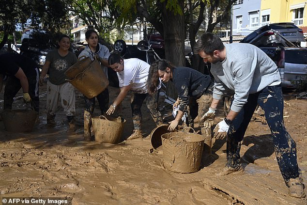 People remove mud from the street on November 1, 2024 after the devastating effects of flooding in a residential area in the city of Massanassa, Valencia region, eastern Spain