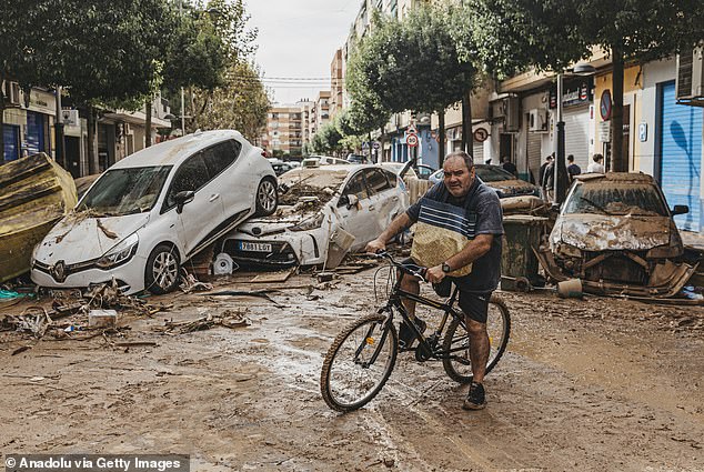 A man rides a bicycle past broken-down cars in the Sedavi neighborhood of Valencia. It is estimated that more than 100,000 homes in the region are currently without power