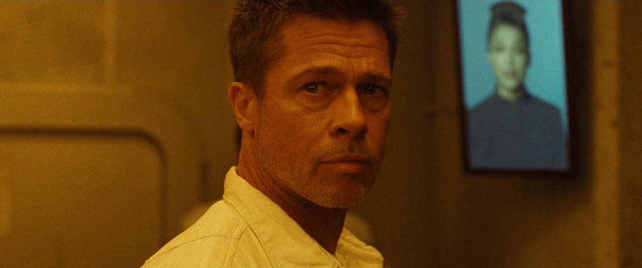 Brad Pitt in a white shirt in a room with a woman on a screen in the background in Ad Astra.