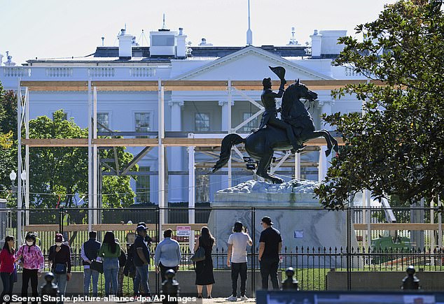 Passersby stand in front of a fence on the White House grounds