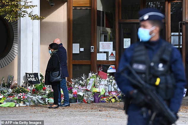 People look at flowers lying outside the Bois d'Aulne secondary school in tribute to murdered history teacher Samuel Paty, who was beheaded by an attacker for showing students cartoons of the Prophet Mohammed in his social studies class, on October 19, 2020 2020 in Conflans. Sainte-Honorine, northwest of Paris. Eight people between the ages of 22 and 65 must appear before the special assize court in Paris from November 4, 2024