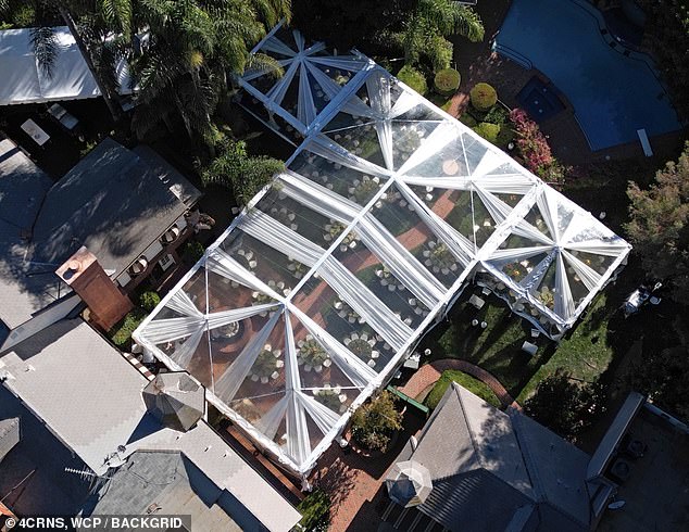 A large tent with a see-through roof was set up behind the house, with several round tables and chairs underneath for the guests