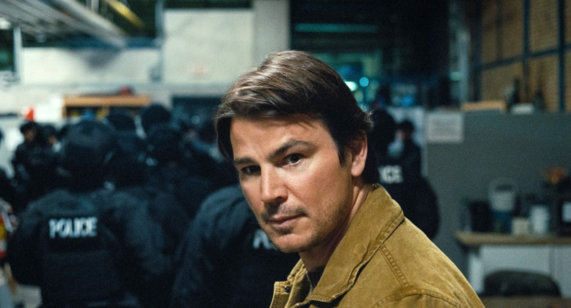 Serial killer Cooper (Josh Hartnett) looks intently over his shoulder as he approaches a group of armored police officers with their backs turned in M. Night Shyamalan's Trap