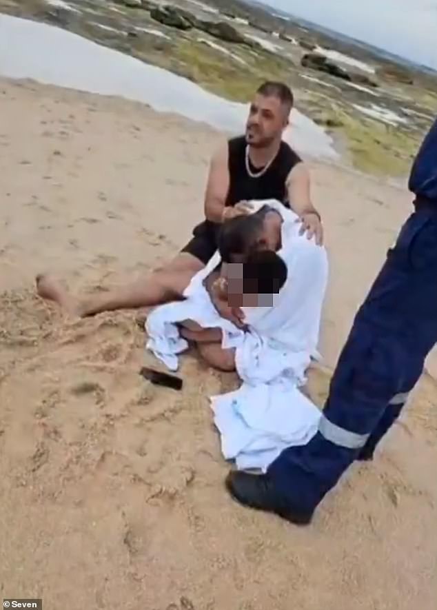 The distraught father was later pictured sitting on the sand and hugging his youngest son tightly as he was comforted