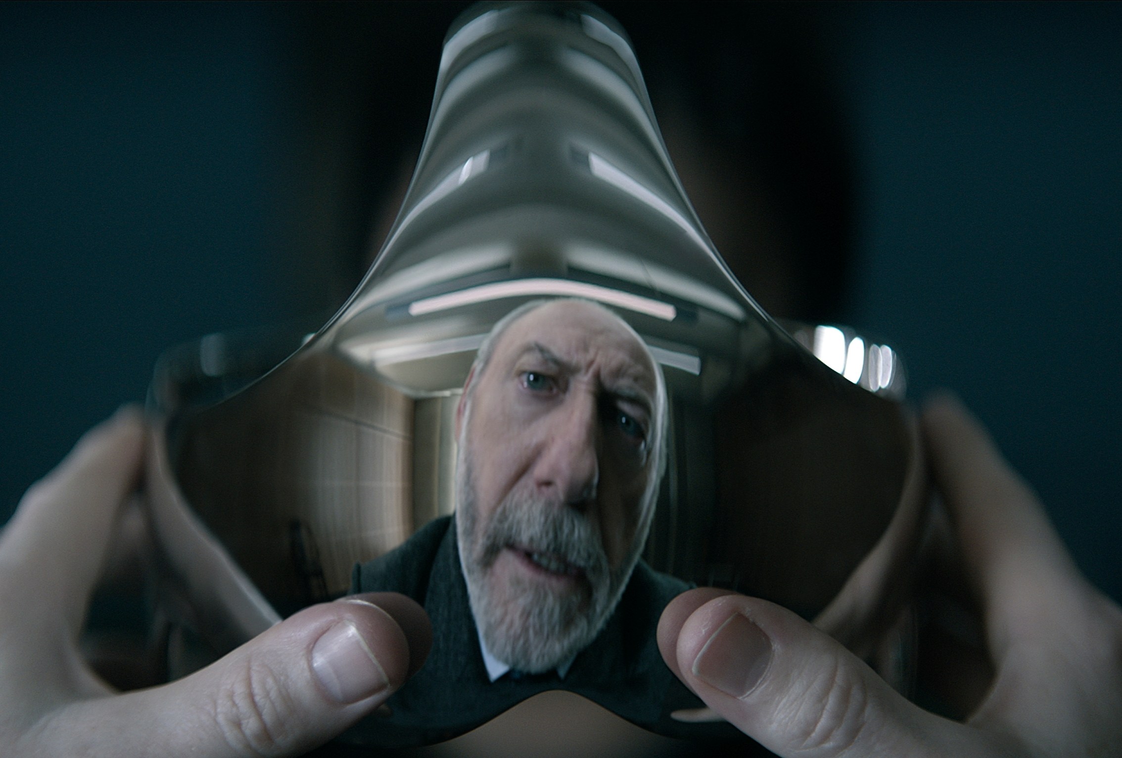 Wade (Liam Cunningham) reflected in the silver visor he holds in his hands