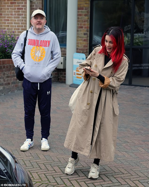 While Dianne Buswell, 35, cut a stylish figure in a beige trench coat as she lounged on her phone before hopping into a car with her dance partner Chris McCausland, 47