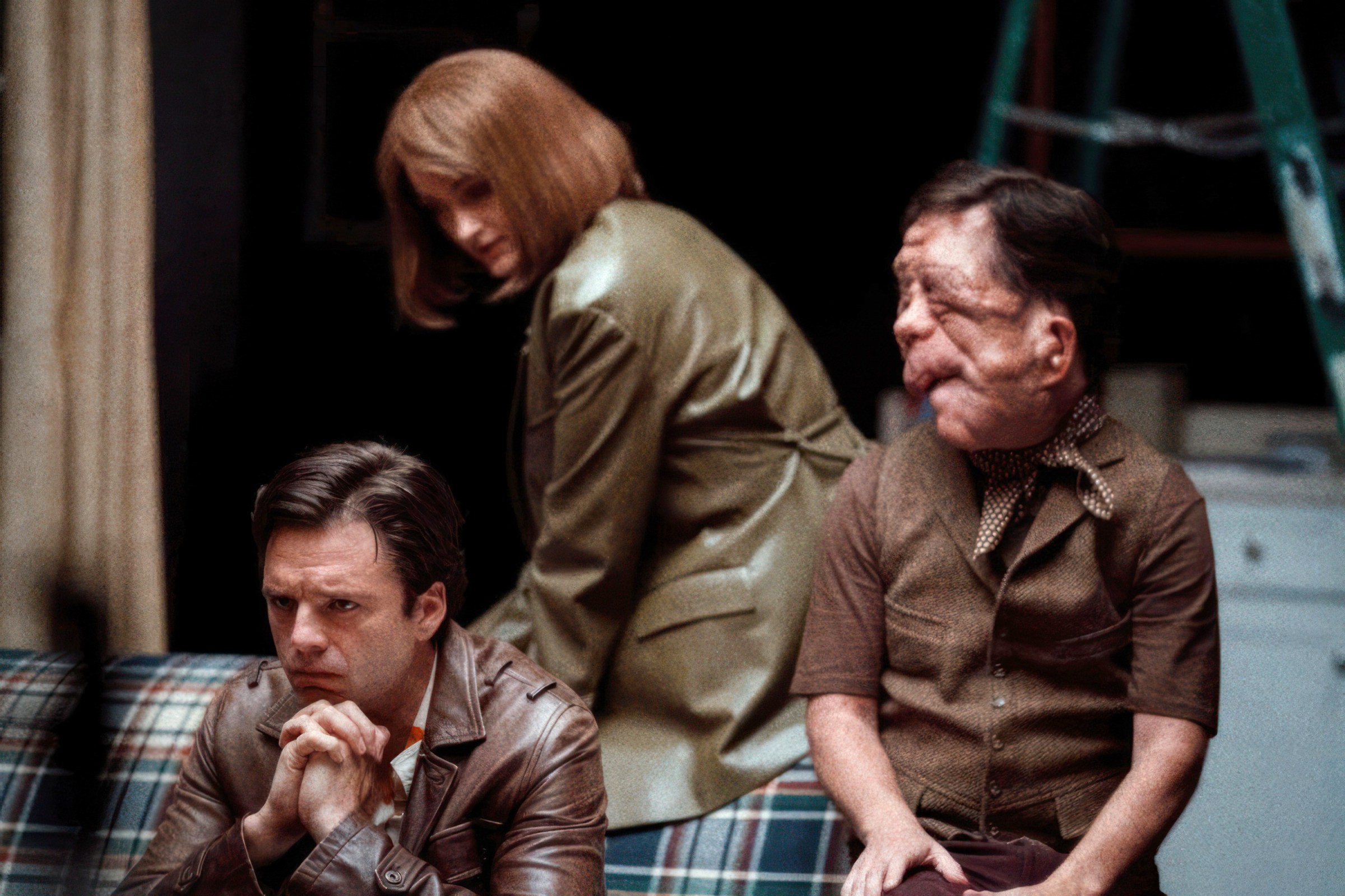 Edward (Sebastian Stan) sits pensively on a couch on a stripped-down theater stage as Ingrid (Renate Reinsve) and Oswald (Adam Pearson) try to comfort him in A Different Man