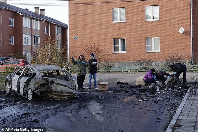 Russian law enforcement officers inspect the wreckage of a drone next to a burnt-out car in the courtyard of residential buildings after a drone strike in the village of Sofyino, Moscow region, on November 10