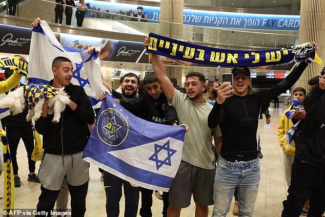 Maccabi Tel-Aviv fans carry flags as they await the arrival of their friends and relatives from Amsterdam at Ben Gurion International Airport