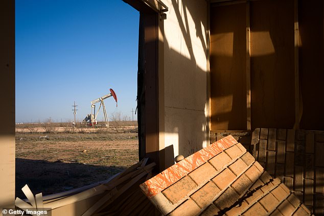 In March, an oil pump jack is shown through the window of a damaged house