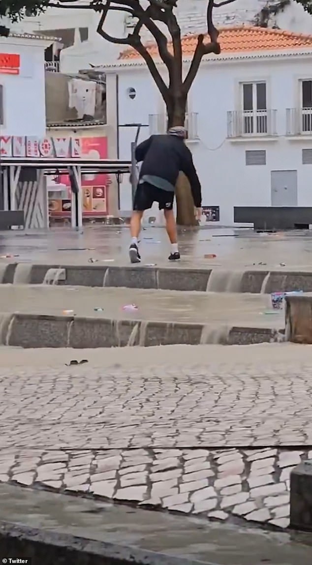 A man is pictured walking through the flash floods in Albufeira, Portugal