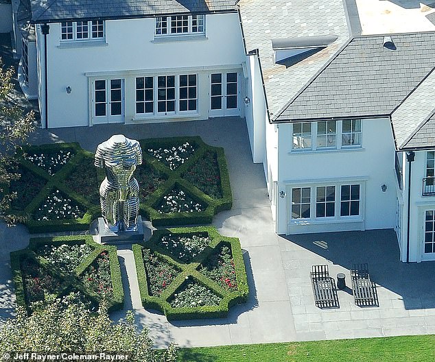 The statue stands between a red and white rose garden with well-groomed hedges