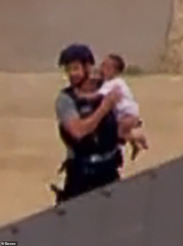 TV helicopter footage captured the dramatic moment the young child was rescued from the home and placed into the waiting arms of an armed police officer (pictured)