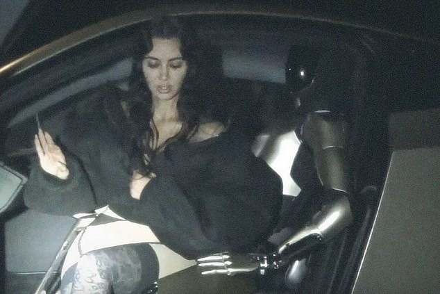 The Kardashians star, 44, went topless under a puffy black jacket and sat on the robot's lap as they posed in the driver's seat of her custom Tesla Model S car