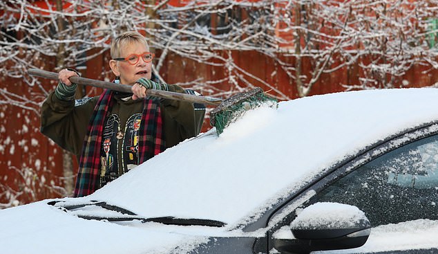 Shannon Finlayson uses a broom to remove snow from the windscreen of her car in Inchbae, Wester Ross in Scotland