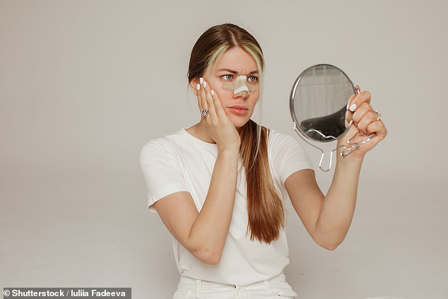 Stock Image: A young woman with a bandage on her nose after rhinoplasty with a mirror in her hand is dissatisfied