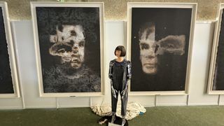 The Ai-Da robot stands in front of her 'AI God' painting on Alan Turing