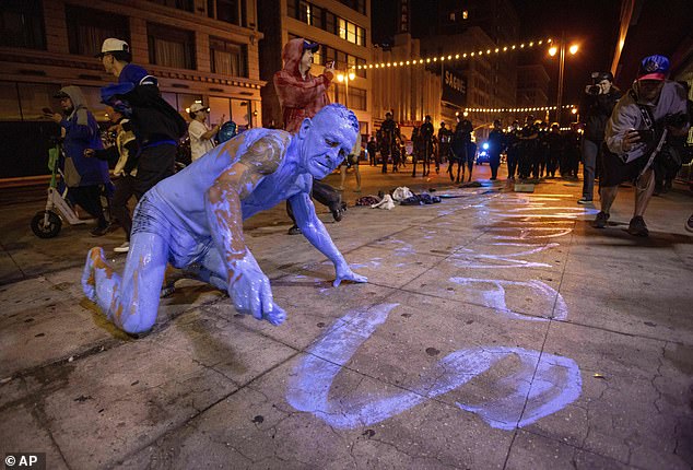 A man covered in blue paint scribbles a message on the streets of LA on Wednesday night