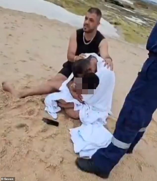 The distraught father is seen hugging his youngest son shortly after his eldest was swept into the sea on Sunday afternoon.