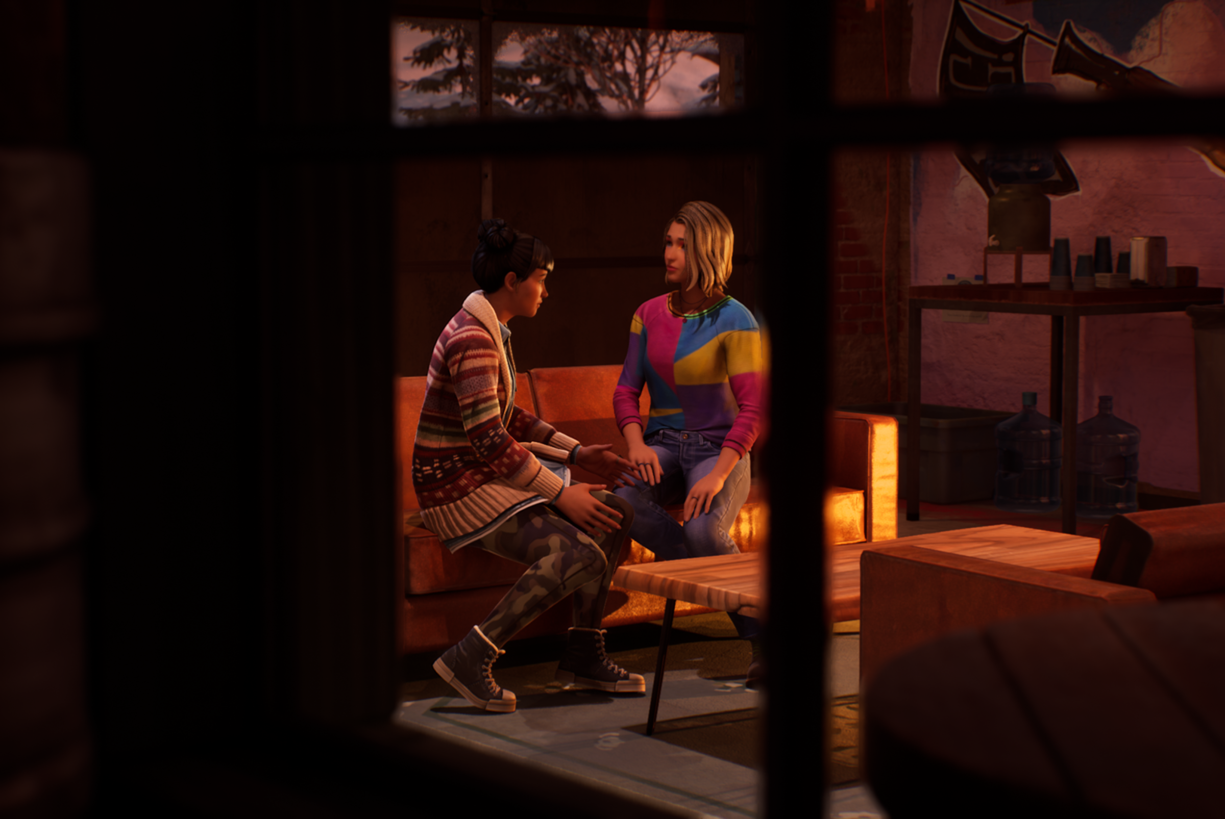 Two characters from Life Is Strange: Double Exposure are sitting on a couch talking to each other. The viewer sees this image from outside the building the characters are in, through a window.