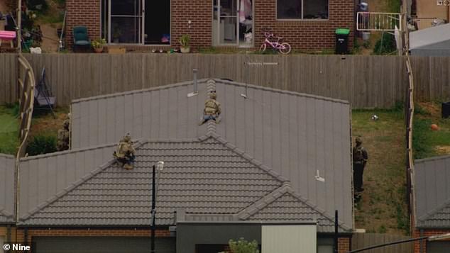 Footage from a news helicopter shows two armed personnel, dressed in green fatigues, on a roof opposite a neighboring house during the siege on Tuesday (pictured)