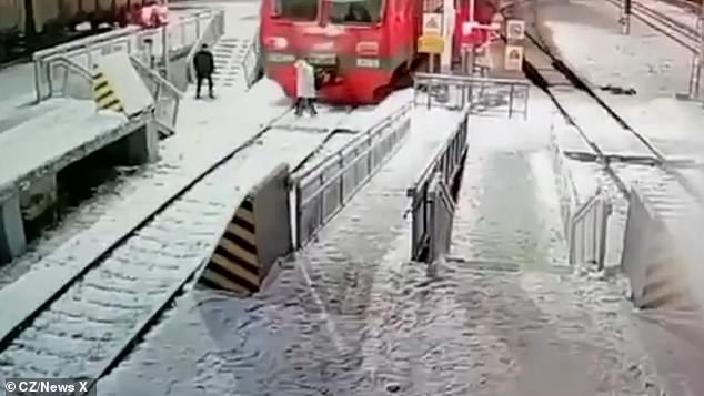 The moving footage shows a woman walking along the train tracks wearing headphones, seemingly oblivious to the train rapidly approaching her.