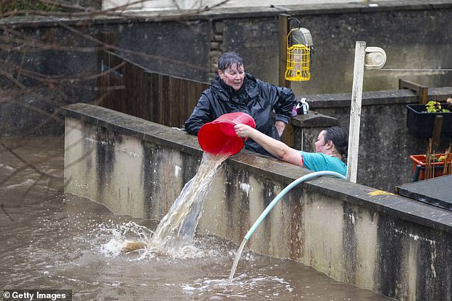 People pour water from the front garden in Pontypridd, Wales, as officials declare a major incident due to river flooding