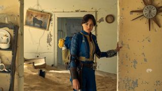 Ella Purnell as Lucy, wearing a blue and yellow suit, looking around an abandoned house in Fallout.