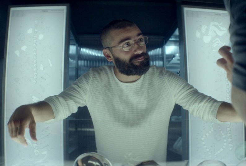 Oscar Isaac stands in front of two bright white lights while wearing a white shirt in Ex Machina