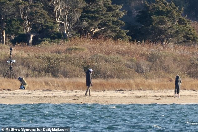 Ashley Biden (left) bends down to pick something up from the beach as Jill Biden (right) looks on and a Secret Service agent (center) stands guard