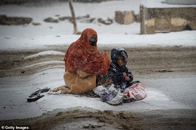 An Afghan woman begs for money as she passes cars in the snow, with a child huddled next to her, on the Kabul road south to Pul-e Alam, Afghanistan, on January 17, 2022