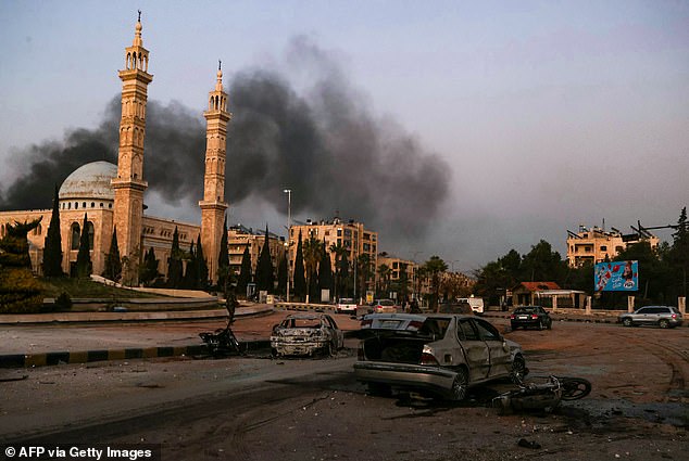 Clouds of smoke in the distance as damaged cars are seen at the site of Syrian regime airstrikes on anti-regime fighters in Aleppo, northern Syria on November 30, 2024