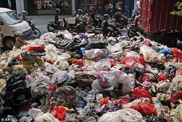 Motorists pass trash, mostly plastic, piled up on the side of a road in Jakarta, Indonesia