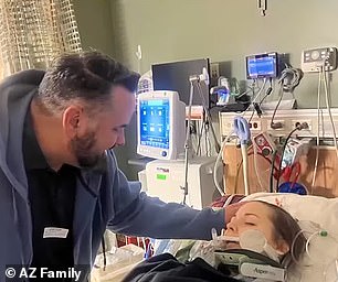 Dad, Brent Wilhite places a soothing hand on his daughter's head as she recovers in the hospital