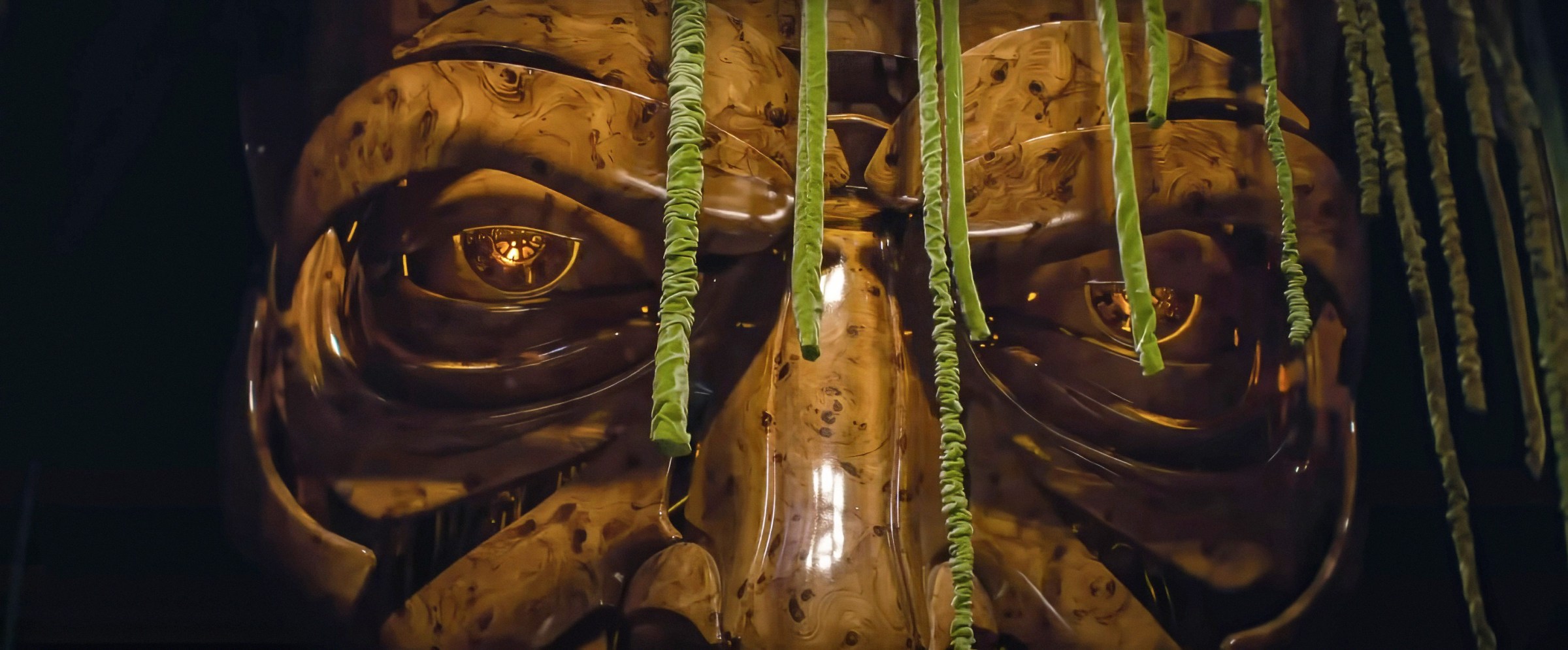 The Wizard of Oz's giant talking mask, seemingly made of highly polished pieces of wood joined together to form an angry-looking face, seen in close-up in Wicked: Part I