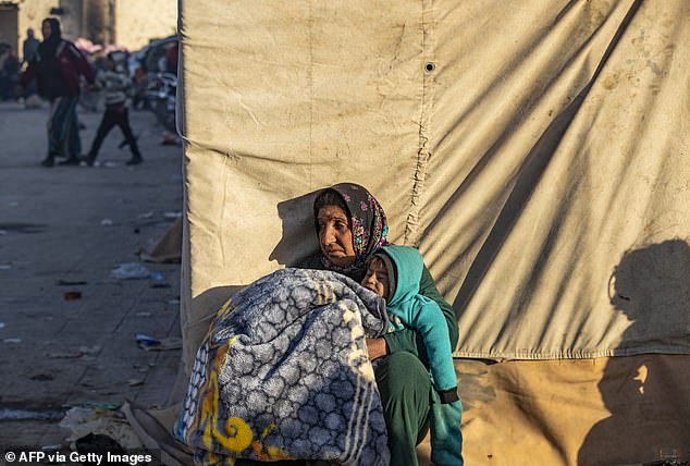 A Syrian Kurdish woman, fleeing northern Aleppo, waits with a child on the street as she arrives in Tabqa, on the western outskirts of Raqa, on December 4, 2024