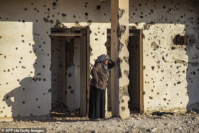 A Syrian Kurdish woman, fleeing from northern Aleppo, stands leaning on a bullet-riddled wall as she arrives in Tabqa, on the western outskirts of Raqa, on December 4, 2024