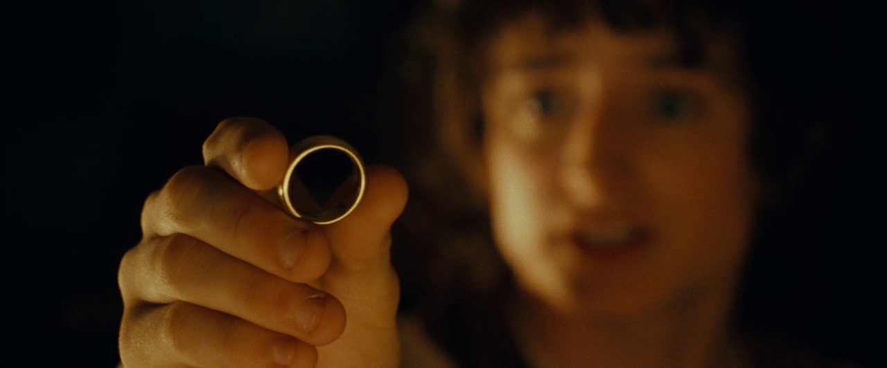 Frodo, out of focus in the background, holds up the One Ring in Peter Jackson's The Fellowship of the Ring