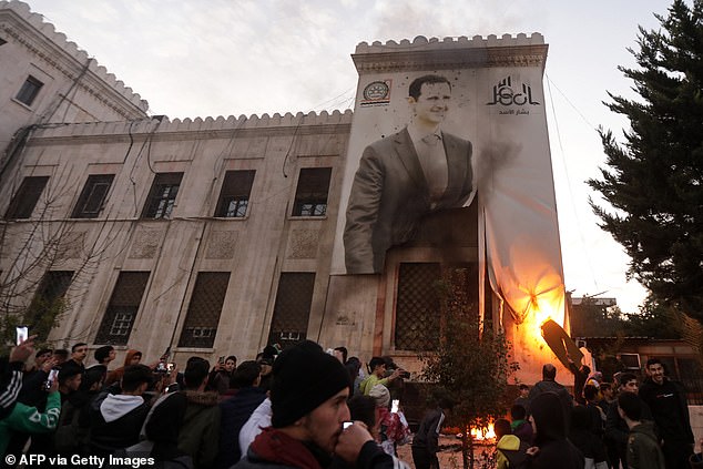 Residents of Hama set fire to a large banner depicting Syrian President Bashar al-Assad hanging from the facade of a municipal building