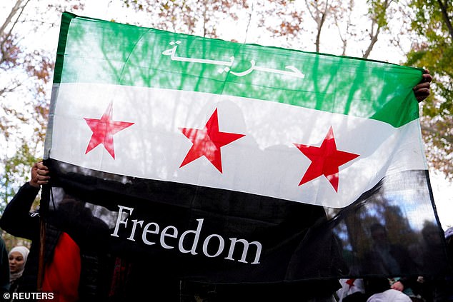 A person holds a Syrian opposition flag with the word "Freedom" during a demonstration celebrating the fall of Bashar al-Assad's regime outside the Syrian embassy in Madrid