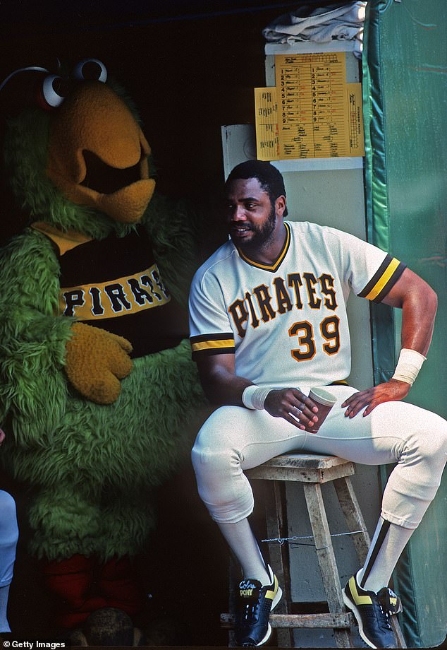 Dave Parker sits on a stool as team mascot Pirate Parrot watches in the dugout